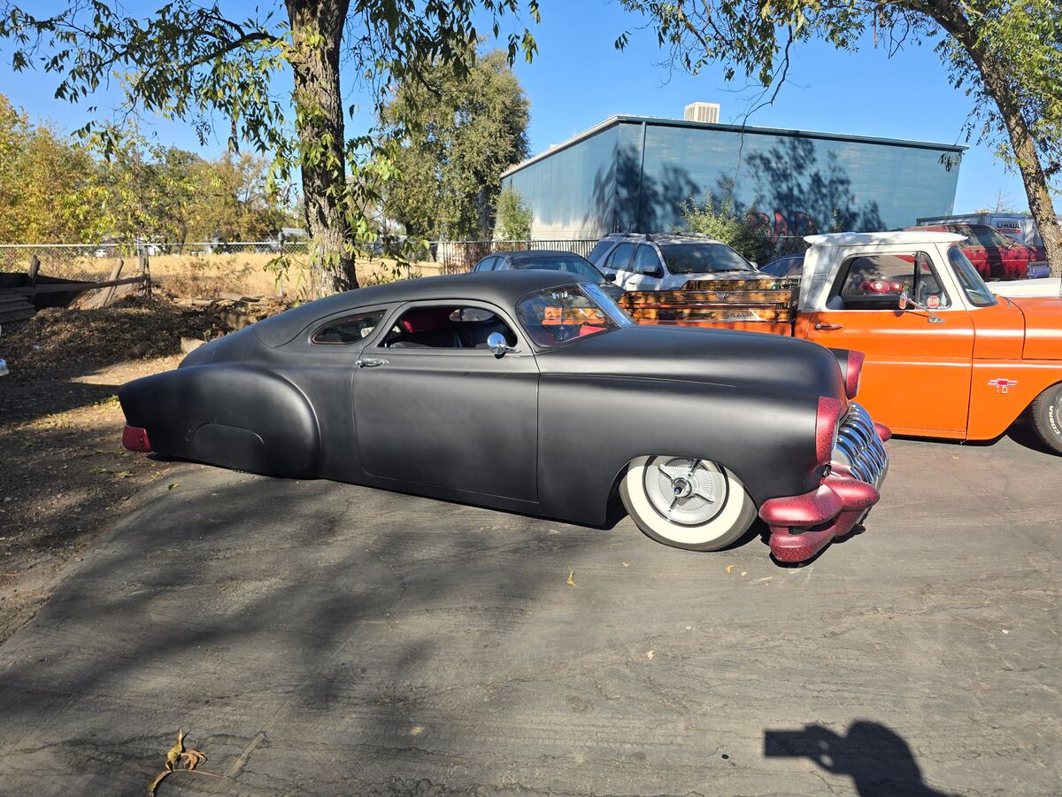 Low black chopped custom with whitewalls beside an orange pickup