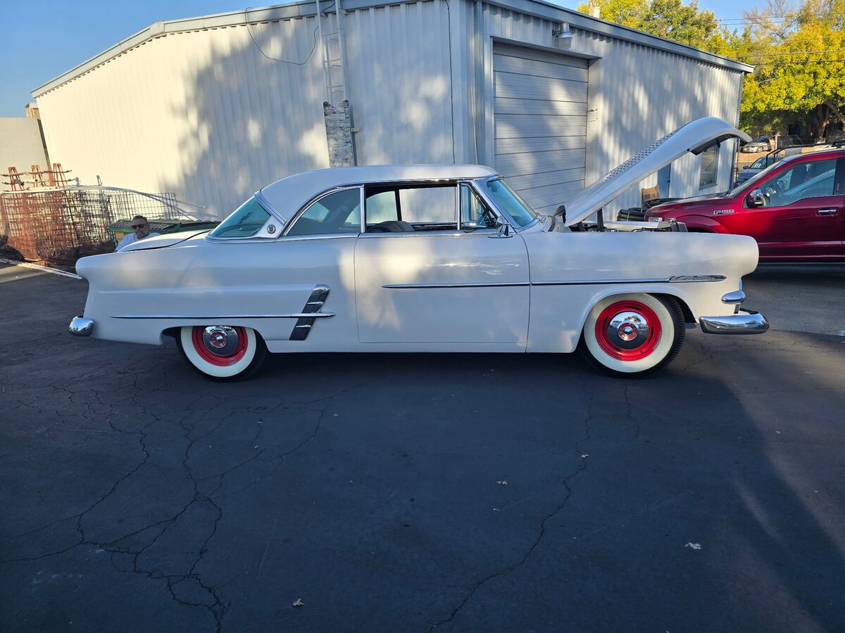 White classic Chevrolet with red wheels parked beside a pickup